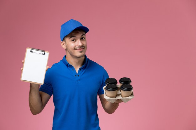 corriere maschio in uniforme blu che tiene le tazze di caffè di consegna e il blocchetto per appunti sulla consegna rosa, uniforme del servizio del lavoratore di lavoro