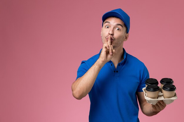 corriere maschio in uniforme blu che tiene le tazze di caffè di consegna in posa sulla consegna del lavoro di servizio rosa, uniforme