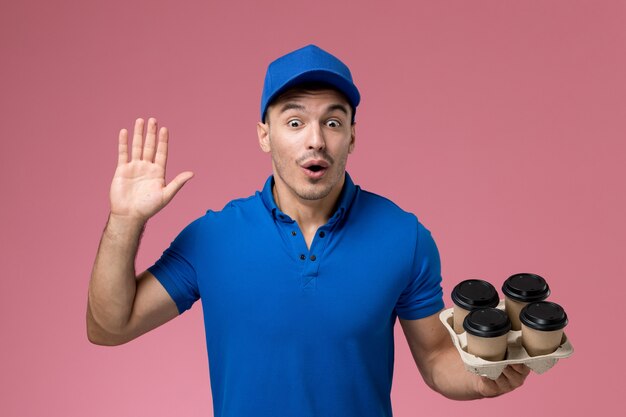 corriere maschio in uniforme blu che tiene le tazze di caffè di consegna marroni sulla consegna di servizio dell'operaio di lavoro rosa e uniforme