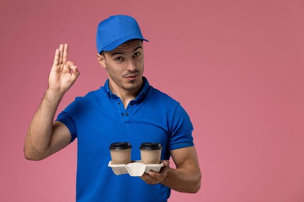 corriere maschio in uniforme blu che tiene tazze di caffè in posa sulla consegna del servizio rosa, uniforme