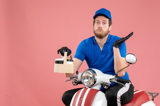 Corriere maschio vista frontale in uniforme blu seduto in bici e tenendo il caffè sul rosa