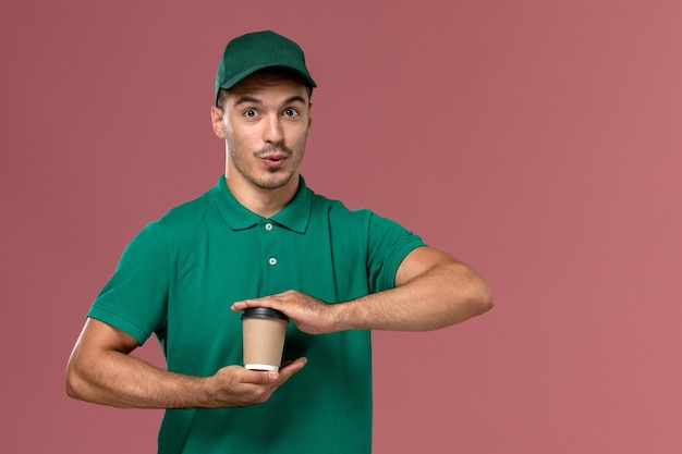 Corriere maschio vista frontale in uniforme verde che tiene la tazza di caffè di consegna sullo sfondo rosa chiaro