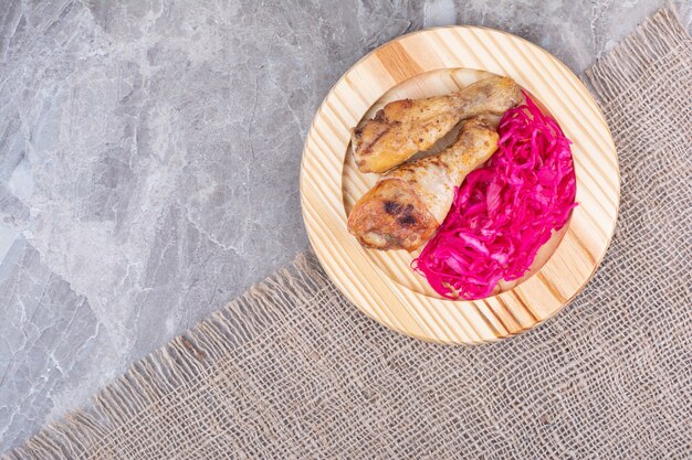 Cosce di pollo alla griglia e cavolo marinato sul piatto di legno.