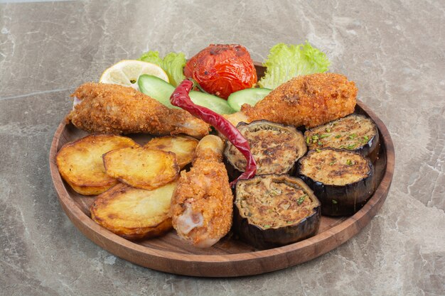 Cosce di pollo fritte con patate e melanzane su tavola di legno.