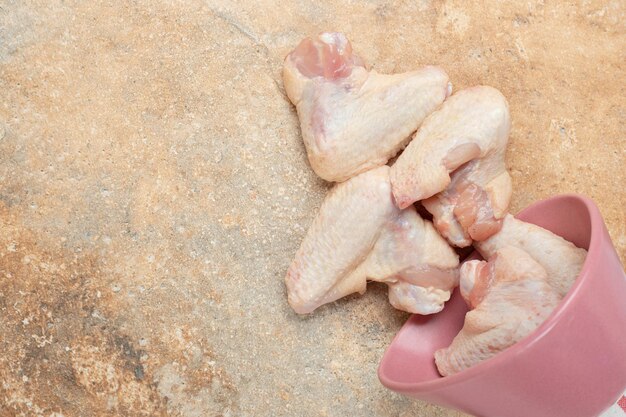 Cosce di pollo impreparate nel piatto rosa sulla superficie di marmo.