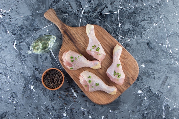 Cosce di pollo su un tagliere accanto a ciotole di olio e spezie, sulla superficie blu.