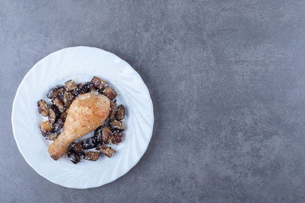 Coscia di pollo alla griglia e melanzane su piatto bianco.