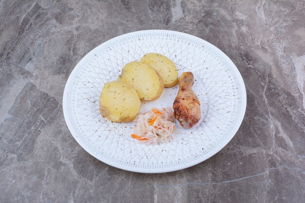 Coscia di pollo alla griglia, patate e crauti sul piatto bianco.