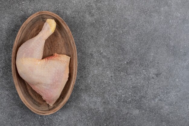 Coscia di pollo cruda. Bacchetta sul piatto di legno.