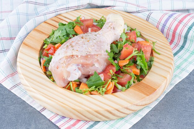 Coscia di pollo crudo e verdure a fette sul piatto di legno.