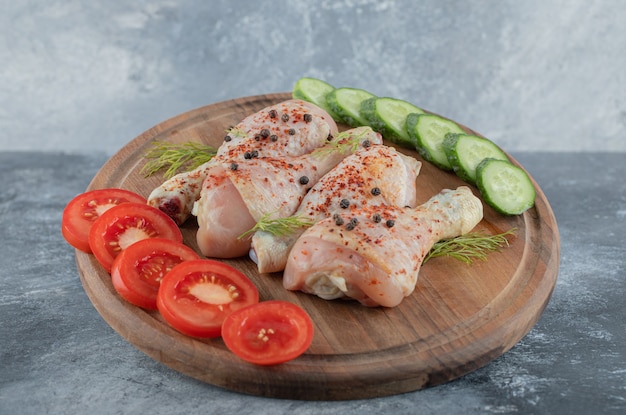 Coscia di pollo crudo marinato su tavola di legno con verdure a fette.