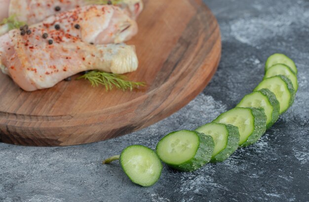 Coscia di pollo crudo su tavola di legno e cetriolo affettato fresco.