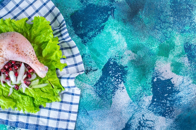 Coscia di pollo marinata con arilli di melograno su foglie di lattuga su una tavola su un canovaccio sullo sfondo blu. Foto di alta qualità