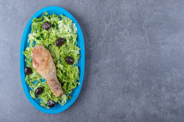 Coscia di pollo, olive e lattuga sul piatto blu.
