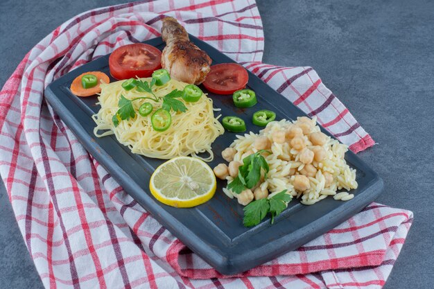 Cosciotto alla griglia, spaghetti e riso su tavola scura.