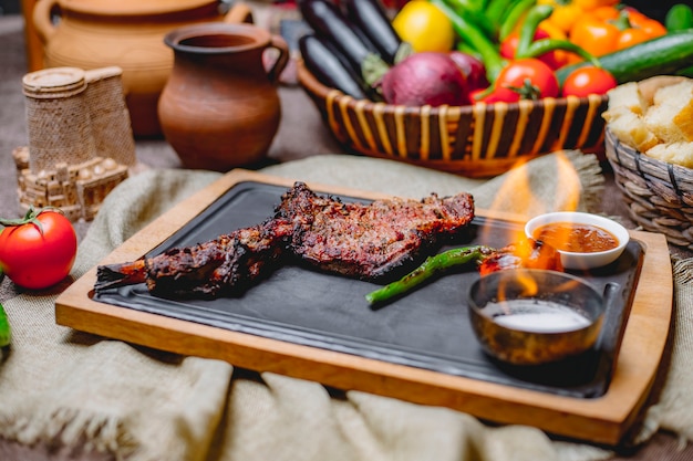 Cosciotto di agnello vista laterale coscia di agnello alla griglia con pomodori e salsa di peperoni verdi caldi alla griglia su un vassoio