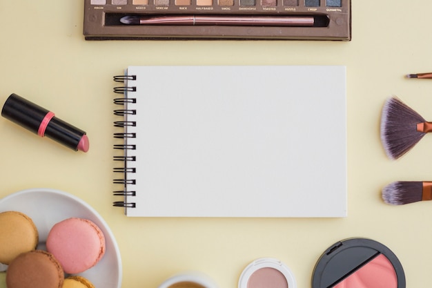 Cosmetici e amaretto con blocco note a spirale in bianco su sfondo beige