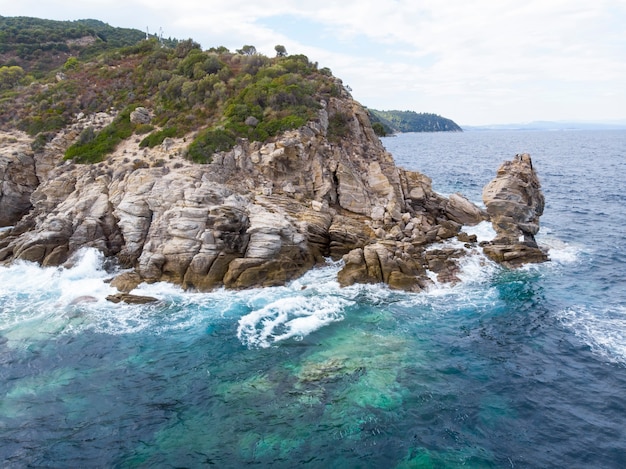 Costa del Mar Egeo con acqua blu trasparente, onde, vegetazione intorno, rocce, cespugli e alberi, vista dal drone Grecia