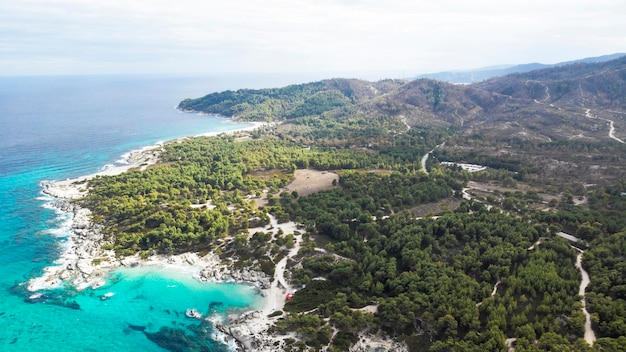 Costa del Mar Egeo con acqua blu trasparente, vegetazione intorno, rocce, cespugli e alberi, vista dal fuco, Grecia