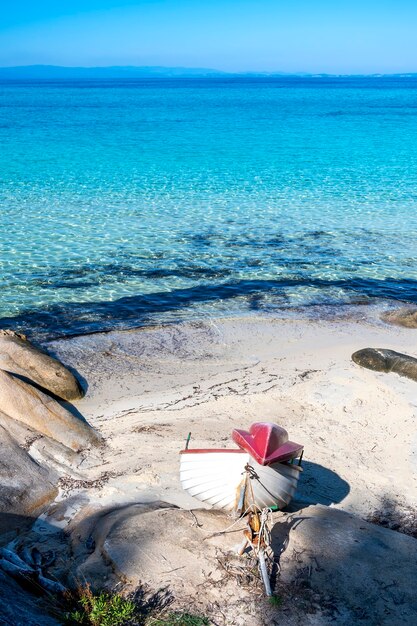 Costa del Mar Egeo con barca spiaggiata, rocce sulla spiaggia, acqua blu, Grecia