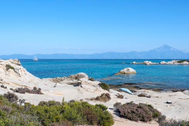 Costa del Mar Egeo con persone che nuotano, rocce sull'acqua e terra con la barca in lontananza, vegetazione in primo piano, acqua blu, Grecia