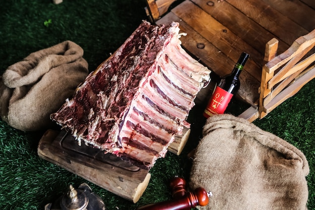 Costole di carne cruda vista dall'alto su un vassoio con una bottiglia di sacchetti di tela da imballaggio vino rosso sull'erba