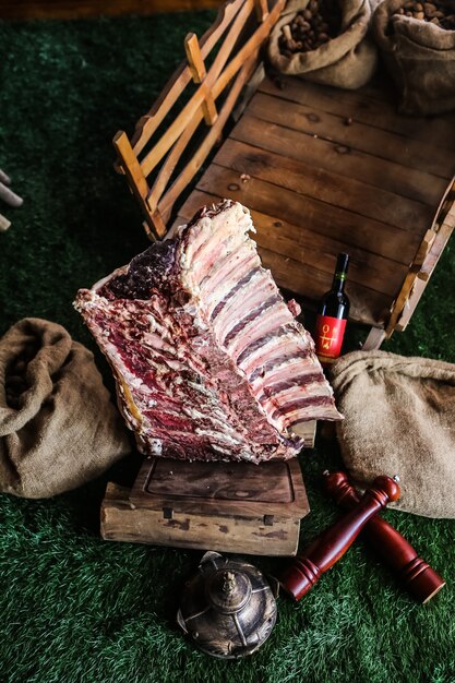 Costole di carne cruda vista dall'alto su un vassoio con una bottiglia di sacchetti di tela da imballaggio vino rosso sull'erba