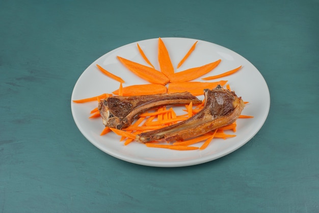Costolette di agnello alla griglia sulla piastra bianca con fette di carota.