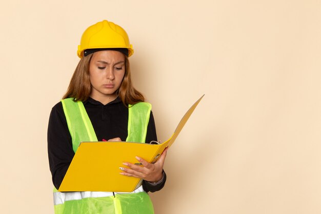 Costruttore femminile di vista frontale in casco giallo che tiene archivio giallo che annota le note sulla parete bianca