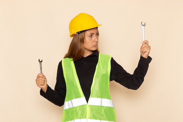 Costruttore femminile di vista frontale in casco giallo che tiene gli strumenti d'argento sull'architetto di costruzione femminile del costruttore dello scrittorio bianco