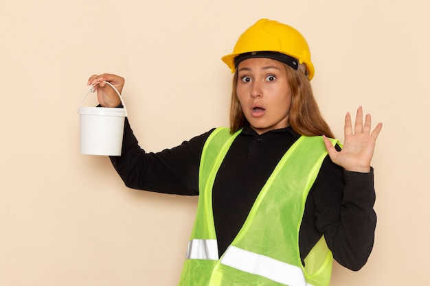 Costruttore femminile di vista frontale in vernice gialla della tenuta del casco sull'architetto femminile della costruzione del costruttore della parete bianca