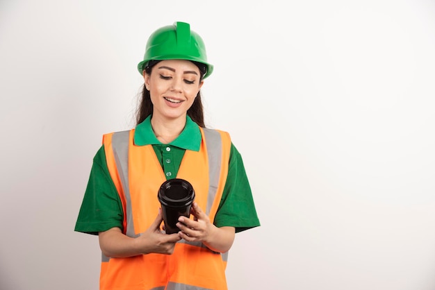 Costruttore femminile sorridente che considera tazza nera. Foto di alta qualità