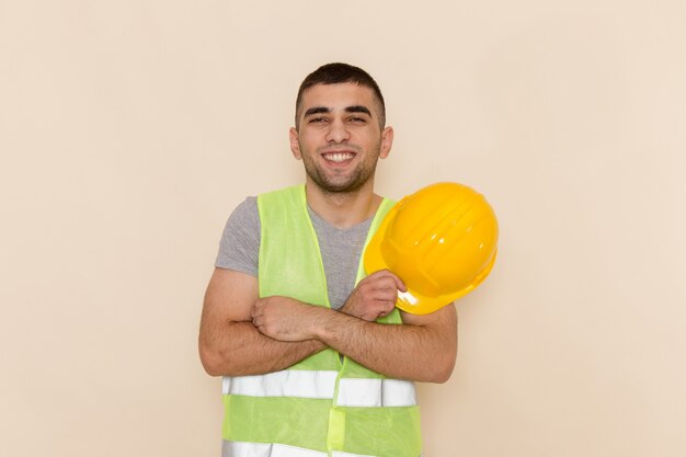 Costruttore maschio di vista frontale che tiene casco giallo sorridente e in posa su sfondo chiaro