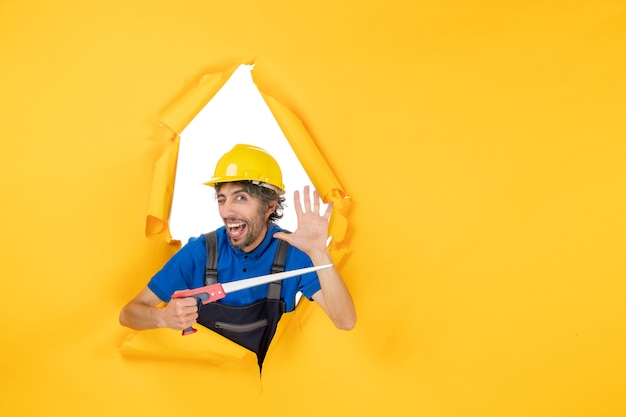 Costruttore maschio di vista frontale in uniforme con lo strumento nelle sue mani sul lavoro di colore del costruttore del lavoro di costruzione della parete gialla