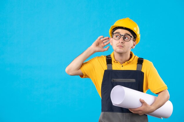 Costruttore maschio di vista frontale in uniforme gialla con piano di carta sull'azzurro