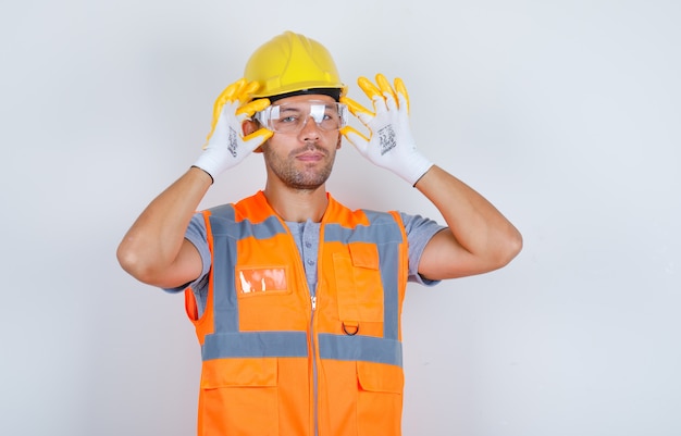 Costruttore maschio in uniforme, casco, guanti con occhiali di sicurezza, vista frontale.