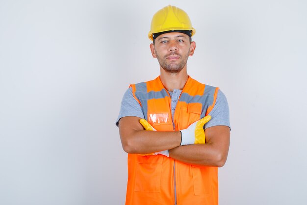 Costruttore maschio in uniforme in piedi con le braccia incrociate e guardando fiducioso, vista frontale.