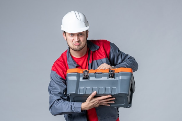 costruttore maschio vista frontale in uniforme che cerca di aprire la cassetta degli attrezzi su sfondo grigio