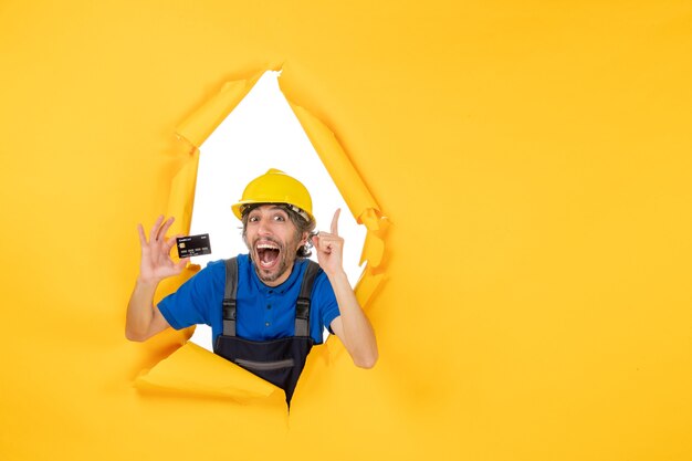 Costruttore maschio vista frontale in uniforme con carta di credito nera su sfondo giallo