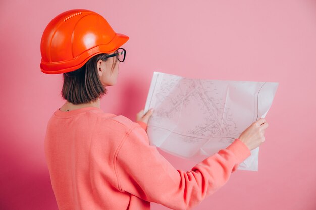 Costruttore sorridente dell'operaio della donna contro fondo rosa. Casco da costruzione.