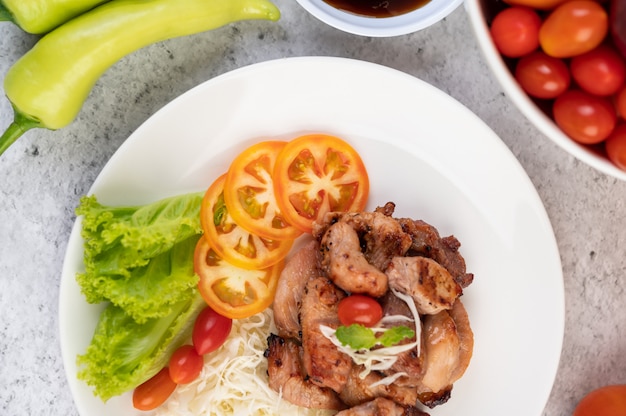 Cotoletta di maiale alla griglia con pomodori e insalata, disposti in un piatto bianco.