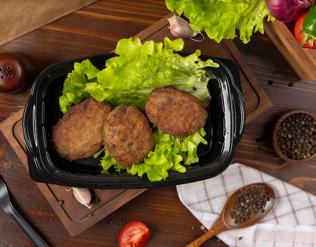 Cotoletta di manzo da asporto servita con lattuga in contenitore nero.