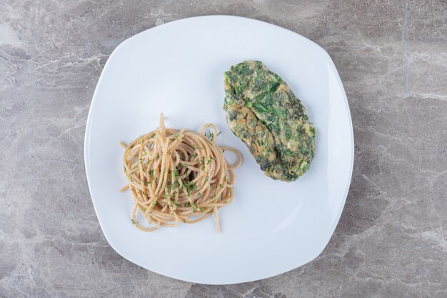 Cotoletta saporita dell'uovo con i verdi e gli spaghetti sul piatto bianco.