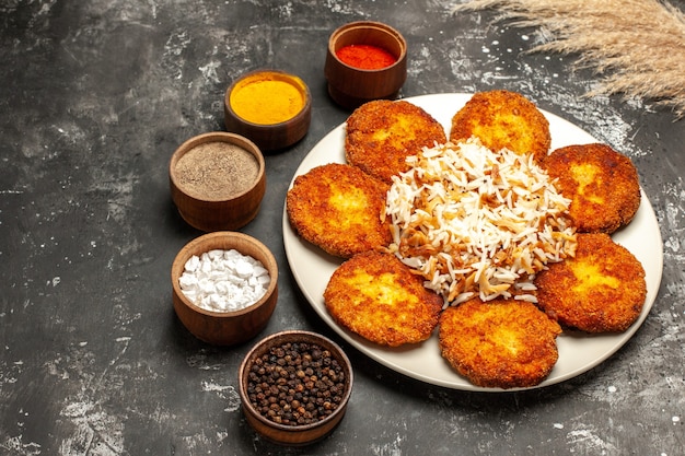 Cotolette fritte di vista frontale con riso cotto e condimenti sulla carne della foto del piatto di superficie scura