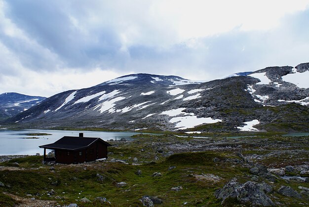 Cottage norvegese rurale vicino al lago circondato da alte montagne rocciose a Atlantic Ocean Road, Norvegia