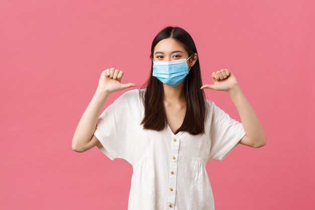 Covid-19, distanza sociale, virus e concetto di stile di vita. Ragazza asiatica orgogliosa e fiduciosa che si vanta di risultati personali, indossando una maschera medica protettiva e un abito estivo, indicando se stessa.