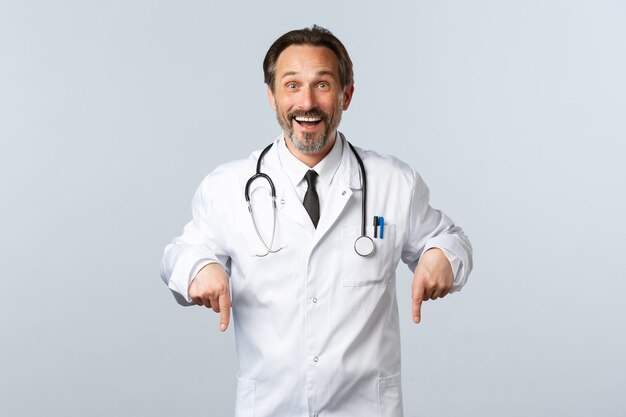 Covid-19, epidemia di coronavirus, operatori sanitari e concetto di pandemia. Medico maschio sorridente felice in camice bianco che invita a fare clic sul collegamento. Terapeuta che mostra la strada alla pubblicità, invitando i pazienti