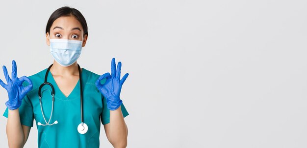 Covid-19, malattia da coronavirus, concetto di operatori sanitari. Medico asiatico eccitato e impressionato, infermiera con maschera medica e guanti di gomma che mostra un gesto corretto, approva o elogia il buon lavoro.
