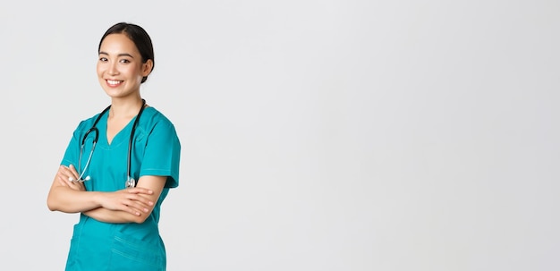 Covid-19, operatori sanitari, concetto di pandemia. Dottoressa asiatica professionista sicura e sorridente, infermiera in camice con stetoscopio per esami, braccia incrociate e sguardo alla fotocamera
