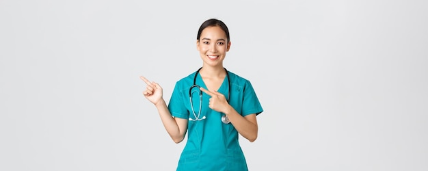 Covid-19, operatori sanitari, concetto di pandemia. Sorridente medico abbastanza asiatico, infermiera in camice e stetoscopio, puntando le dita nell'angolo in alto a sinistra, mostrando il banner della clinica online, sfondo bianco.